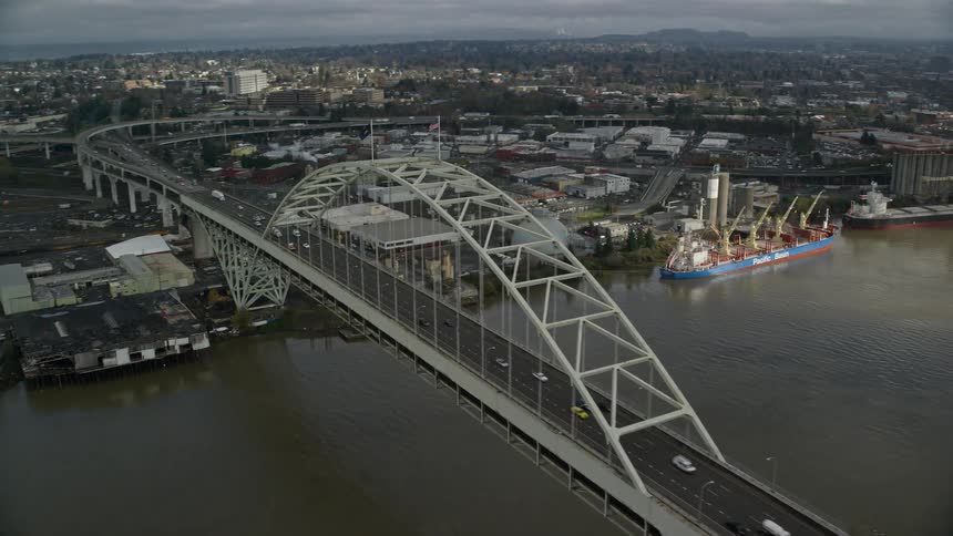 Aerial of a bridge over a river between moving from industrial area to downtown city skyline covered in fog at sunrise