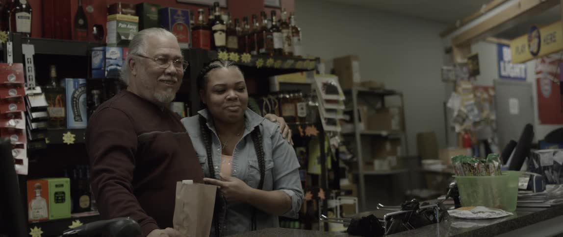 A man and woman pose behind a liquor store counter