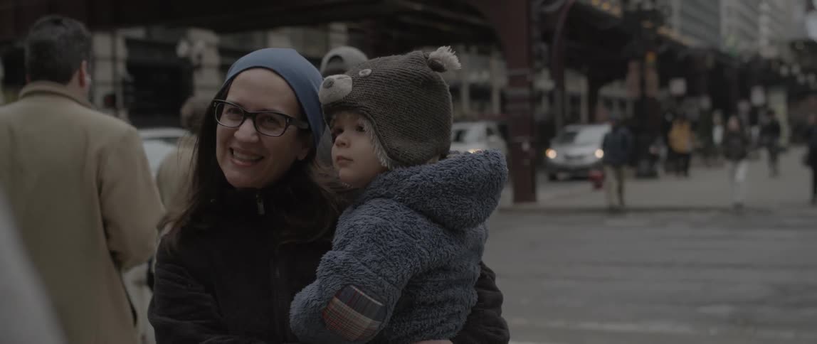 A woman is smiling as she holds a baby near an intersection