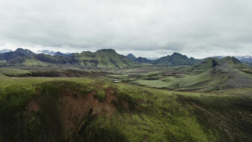 Aerial view of a jeep driving on the ridge of a hill next to the mountains