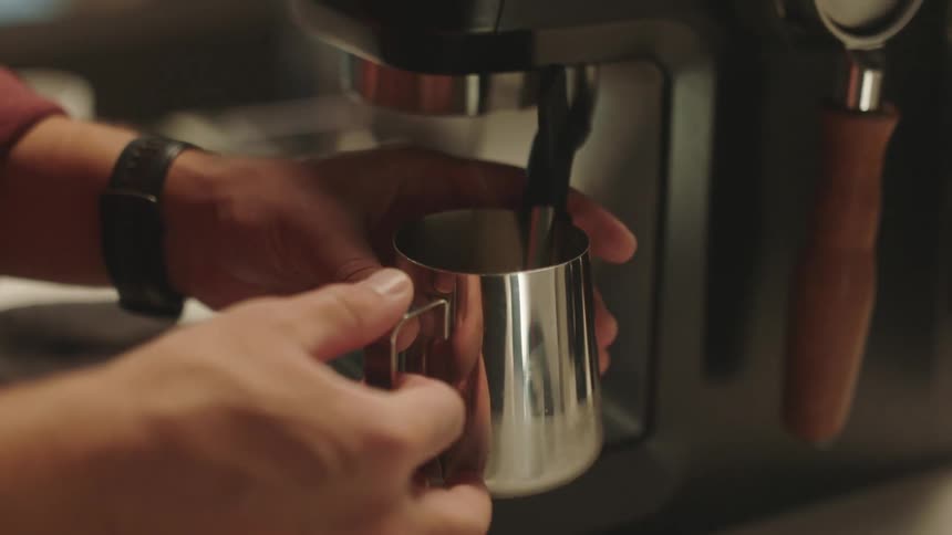 A person holding a cup getting coffee from a coffee maker