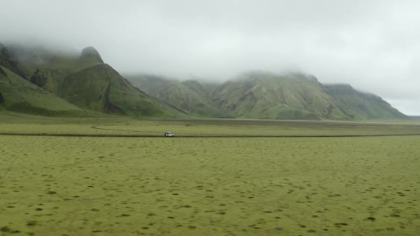 A car in a flat landscape with mountains covered in fog during the day