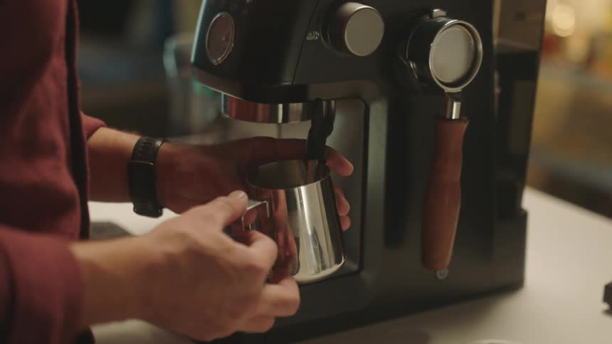 Closeup of a persons hands holding a cup while pouring cappuccino from a machine