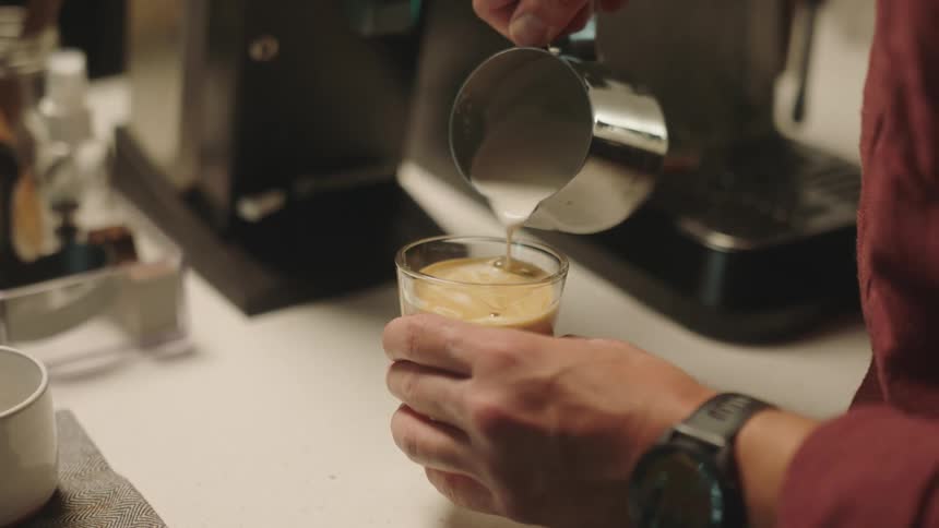 In the hands of a man pouring milk into his espresso coffee