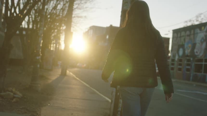 Back view of a female walking on the sidewalk at sunset