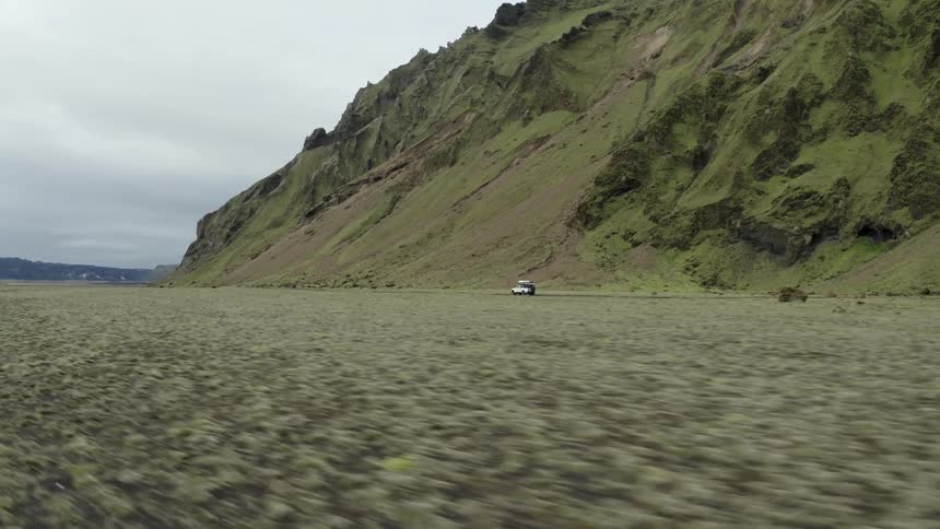 A car driving in a flat landscape with mountains during a cloudy day