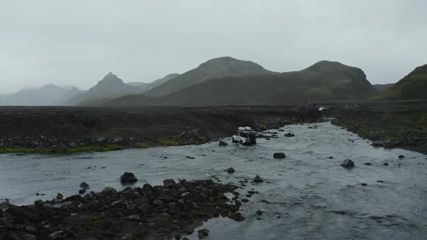 Aerial of a car crossing a river in the mountains landscape