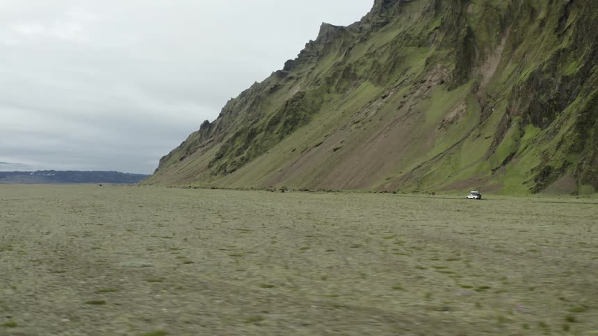 A truck travels along the side of a mountain under a cloudy sky