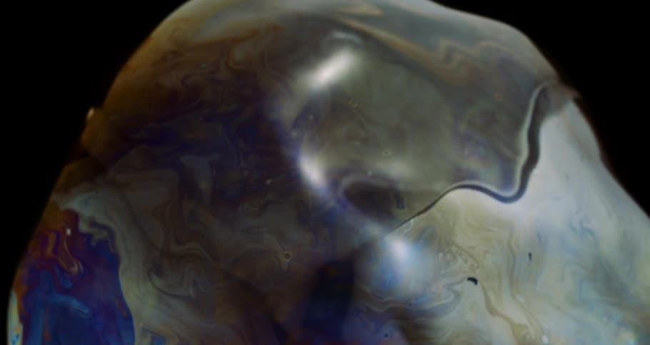 Colorful liquid bubble in extreme closeup on a black background in slow motion