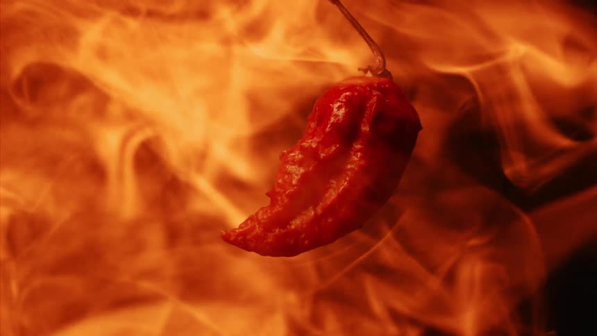A red pepper on a black background surrounded by fire and flames