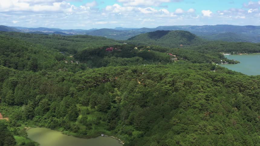 Lush green hills surrounding a body of water with a clear sky above and scattered buildings amongst the trees
