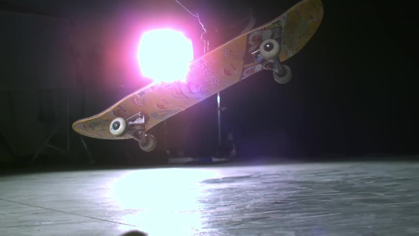 Legs of a person performing skateboard stunt in a room at night