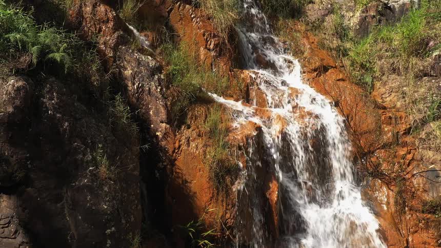 A small waterfall cascading down brown rocks on a bright sunny day