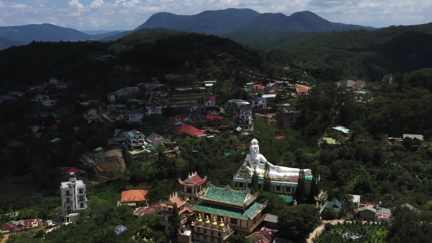 An aerial view of a rural town with several trees and a temple with a statue