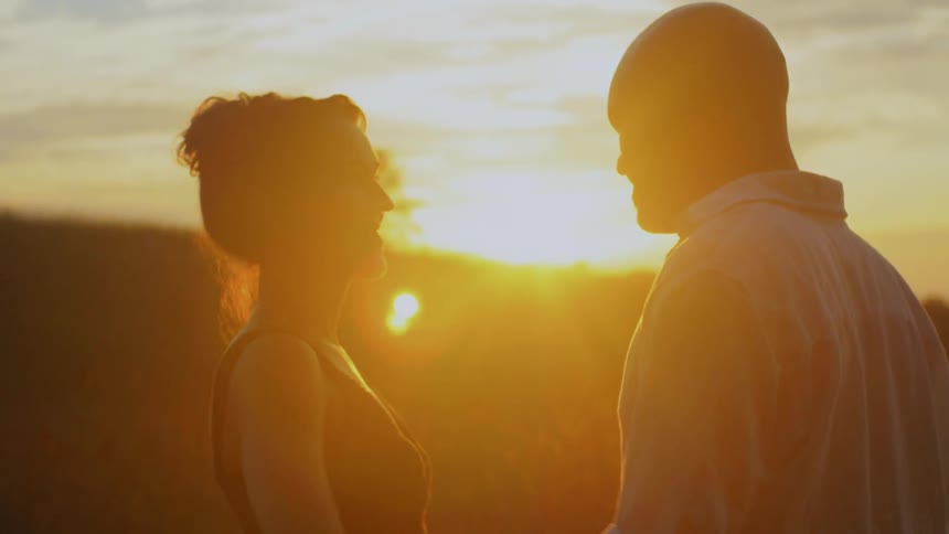 A man is kissing a woman's hand at sunset