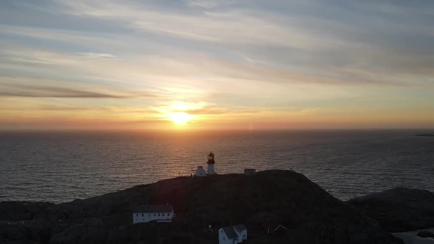 Aerial view of a lighthouse and other houses on a hill on the ocean coast at sunrise