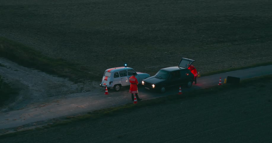 An aerial view of two policemen checking a stopped vehicle on a rural road on farmland at dusk