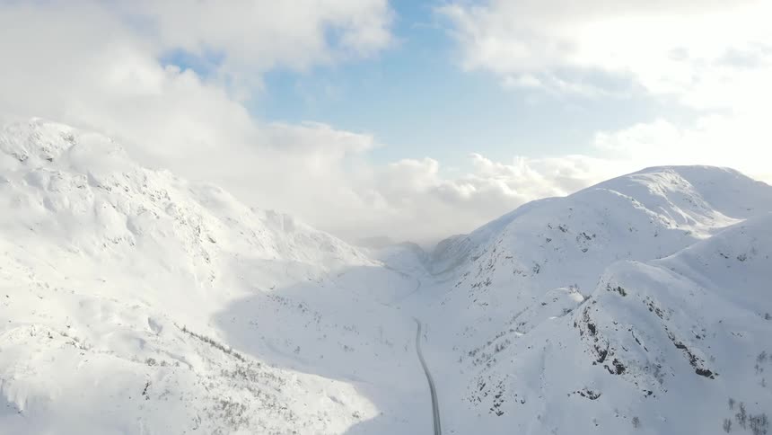 A road runs through a snow covered mountain valley under a cloudy sky