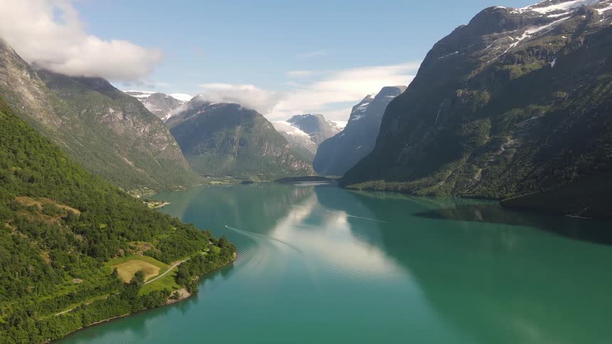 Landscape of a greenish lake surrounded by a chain of snowcapped mountains and vegetation in the daylight
