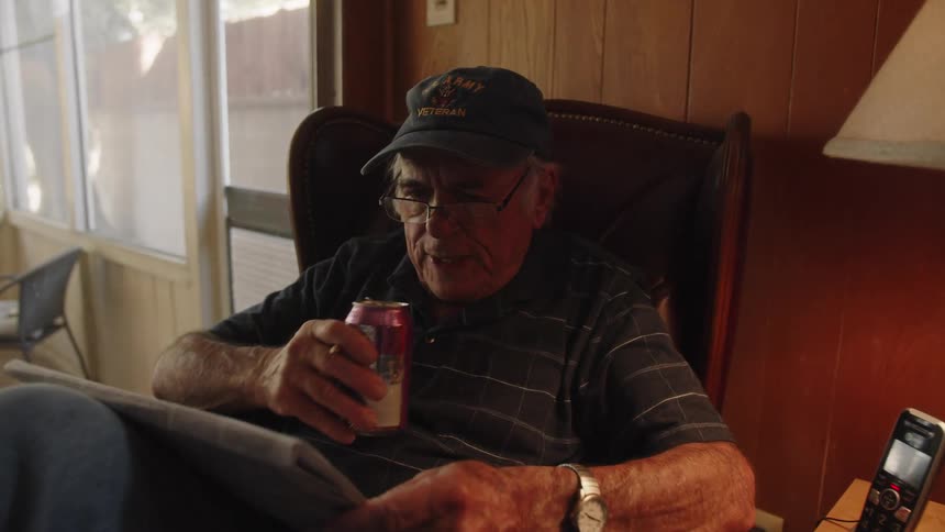 Elderly man drinks beverage while sitting and reading newspaper at home