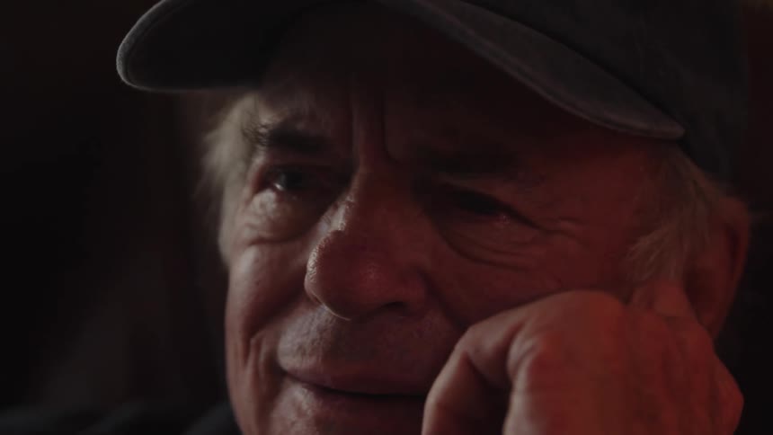 An elderly man wearing a cap becomes emotional and tears up expressing his feelings