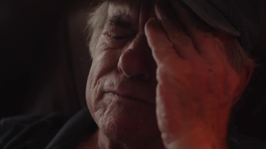 Elderly teary eyed man raises his hand to his face