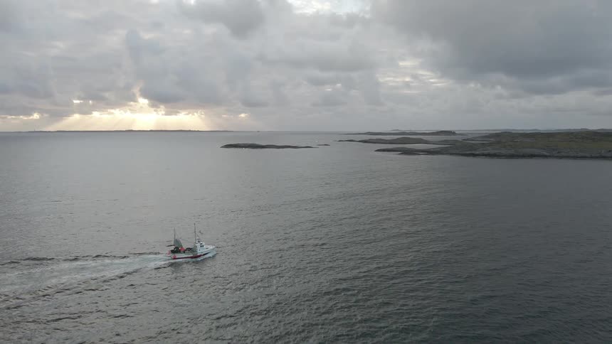 Aerial view of the sea with a boat passing on a cloudy day and the sunrise on the horizon