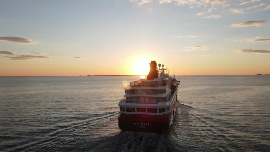 A large boat is sailing on the water and the sun is strong in the sky