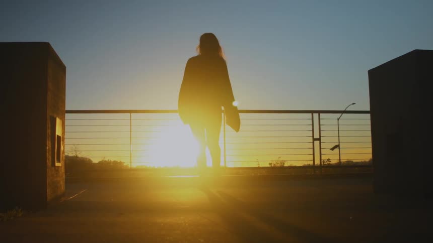 A woman walks over to a railing to watch the sun set