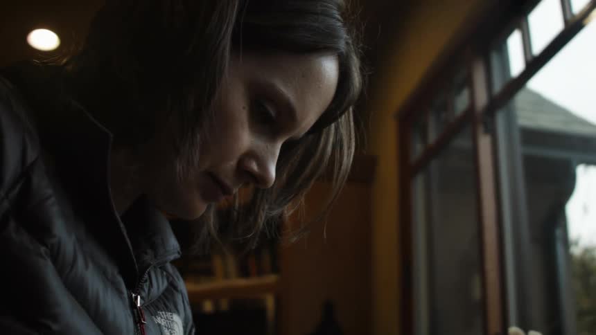 A woman is looking down by a window