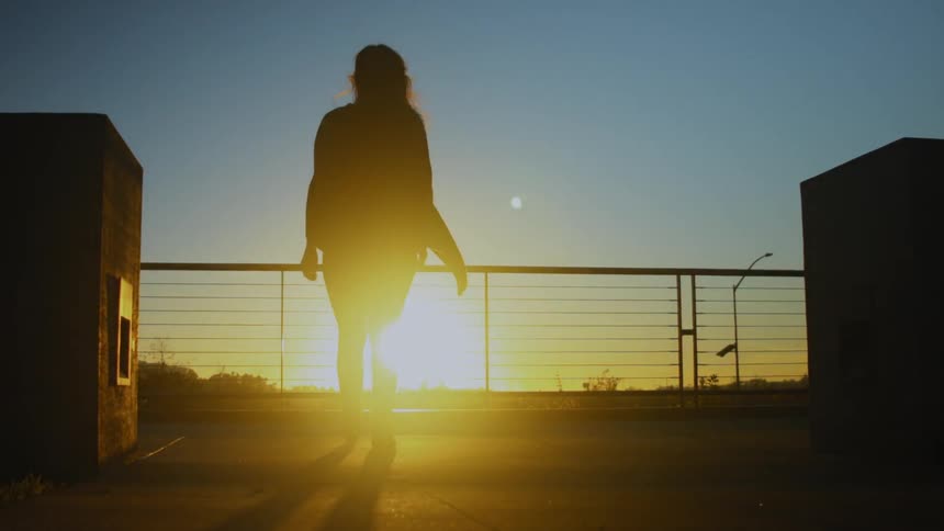 A woman walks over to the railing at sunset on a windy day
