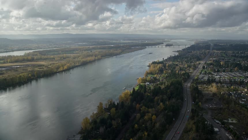 Aerial view of a large river and a highway in a suburban area during a cloudy fall day