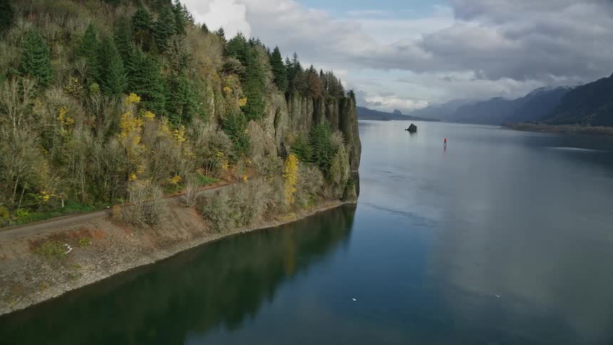 Aerial panorama of a train track under a cavern and beside a lake