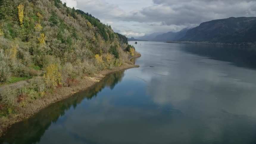 Aerial panorama of a train track amid mountains next to a lake under a cloudy sky