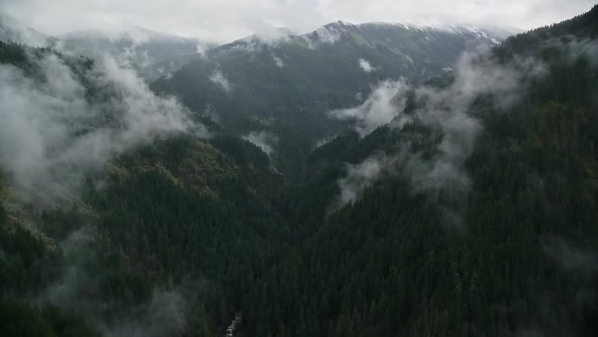 Aerial of a valley between mountains and forests during a cloudy day