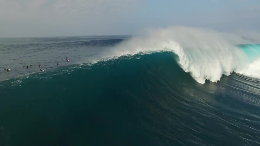 An ocean wave crashes down with swimmers in the distance
