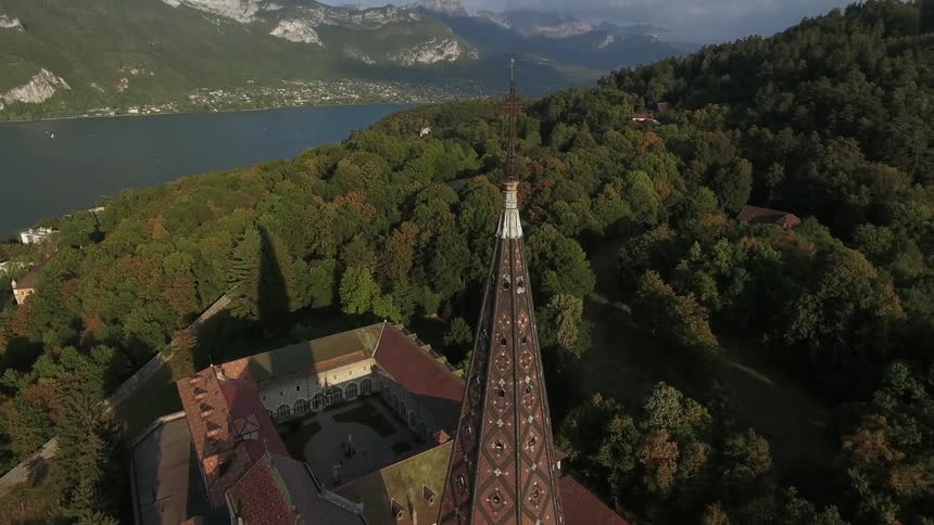 A building in the woods has a tower with a cross at the top