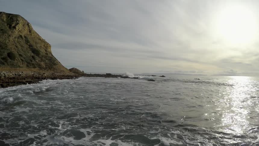 Ocean waves wash ashore as the sun shines overhead