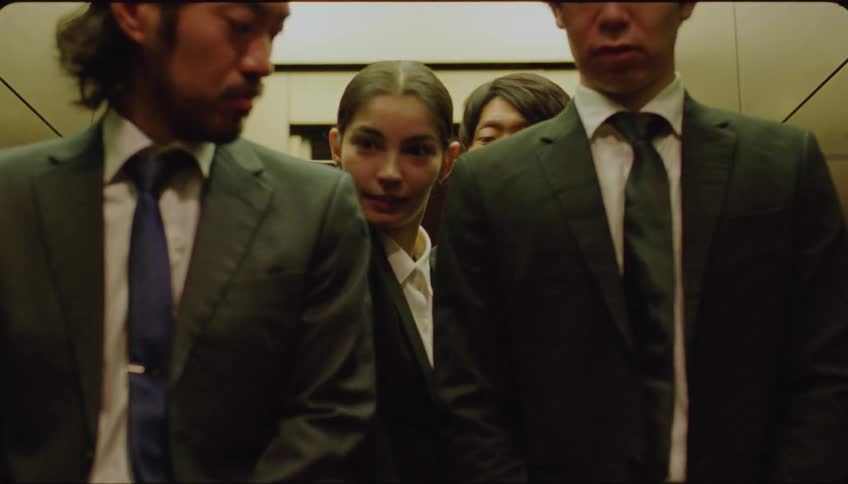 Woman exiting the elevator with three men in suits