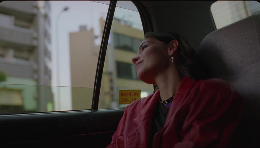 Young woman in the back seat of a taxi with a happy facial expression observing a metropolis on a cloudy day