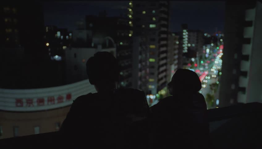 Man and a woman talking while standing at the top of a metropolis building at night