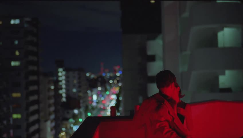 Young man and woman on a building terrace at night talking and flirting and the man takes off his coat and puts it on her