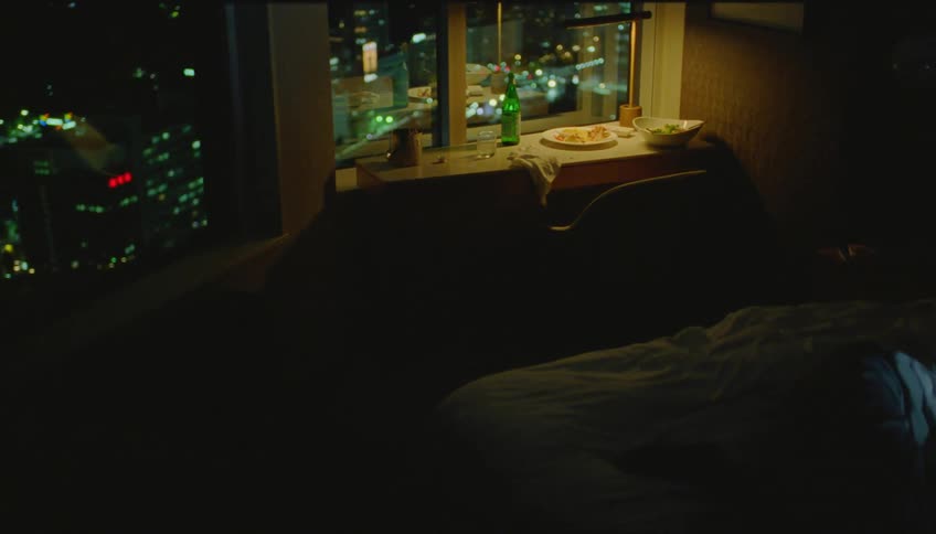 Lady lays on the bed in an apartment watching movies on a laptop at night