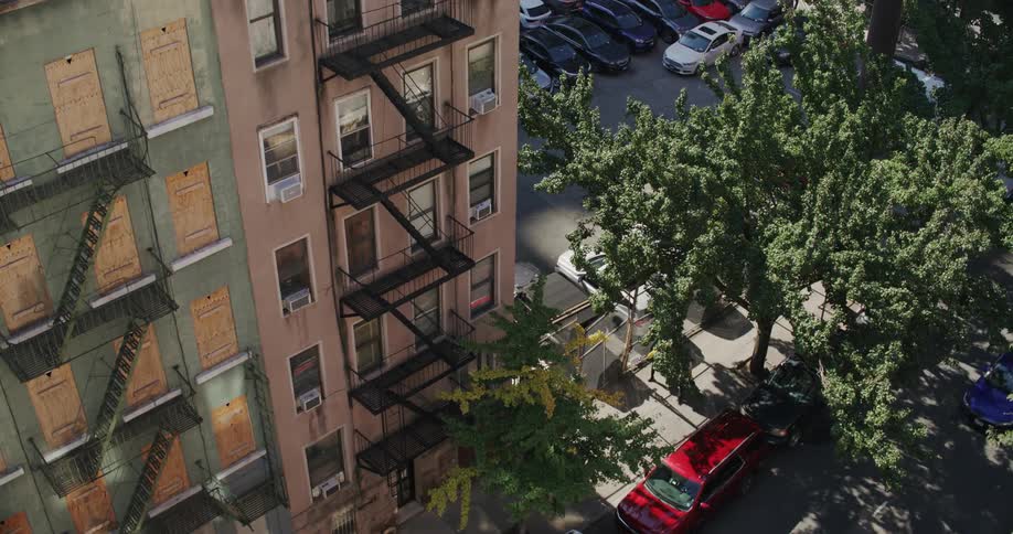 People walk on the sidewalk near an apartment complex with a full parking lot