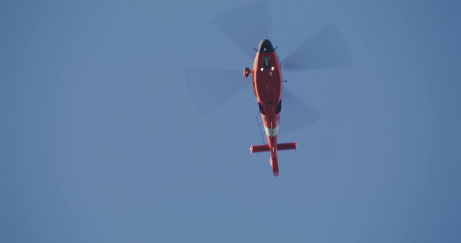 A red helicopter flies in a clear blue sky