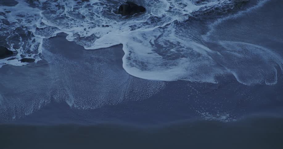 Ocean wave breaking against black sand beach