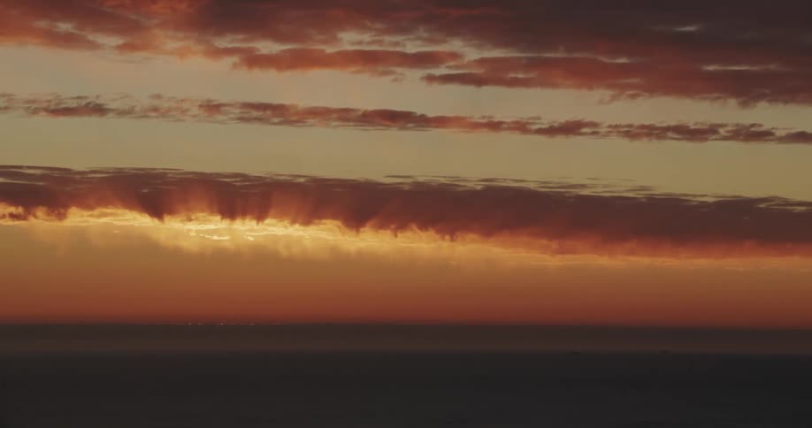 A boat sails under colorful clouds over the water at sunset