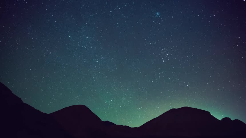 Stars in the night sky move over mountains