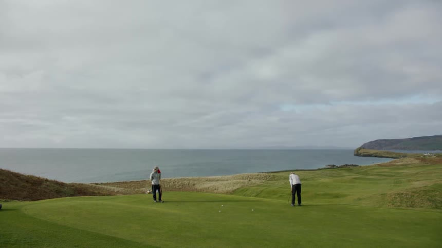 Two people playing golf on a course facing the sea on a cloudy day