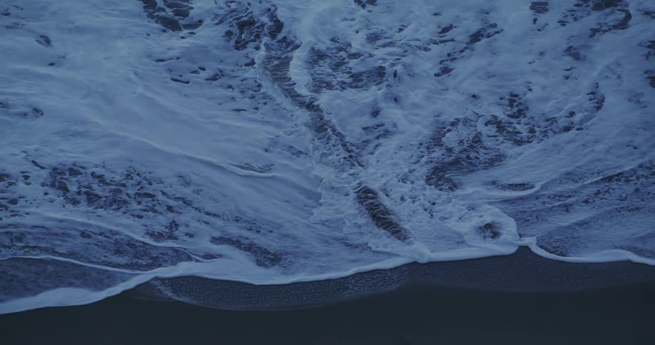 Ocean waves breaking against the black beach